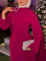Plum modest cape evening dress with white hijab and silver clutch at wedding venue