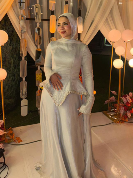 Off-white silver modest peplum evening dress with white hijab and warm wedding lights in the background