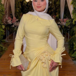 Pastel yellow modest evening dress with long sleeves and draped waist, styled with white hijab in floral wedding venue