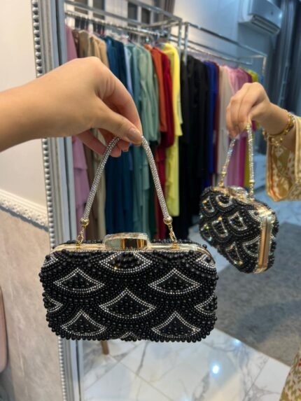 Black beaded evening clutch with silver geometric pattern and gold chain handle displayed in store
